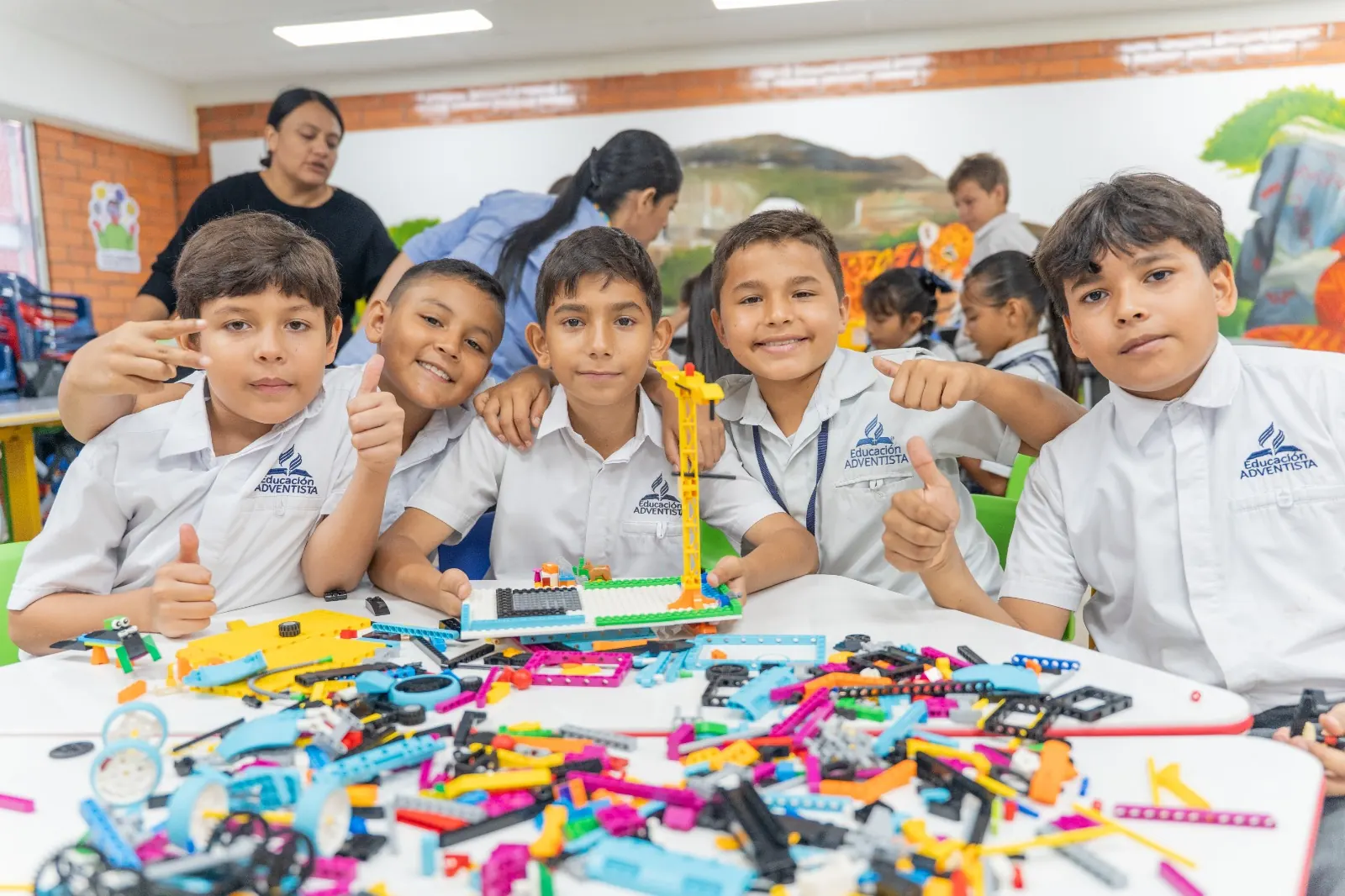 Niños de primaria sonríen alrededor de una mesa llena de piezas y su robot terminado