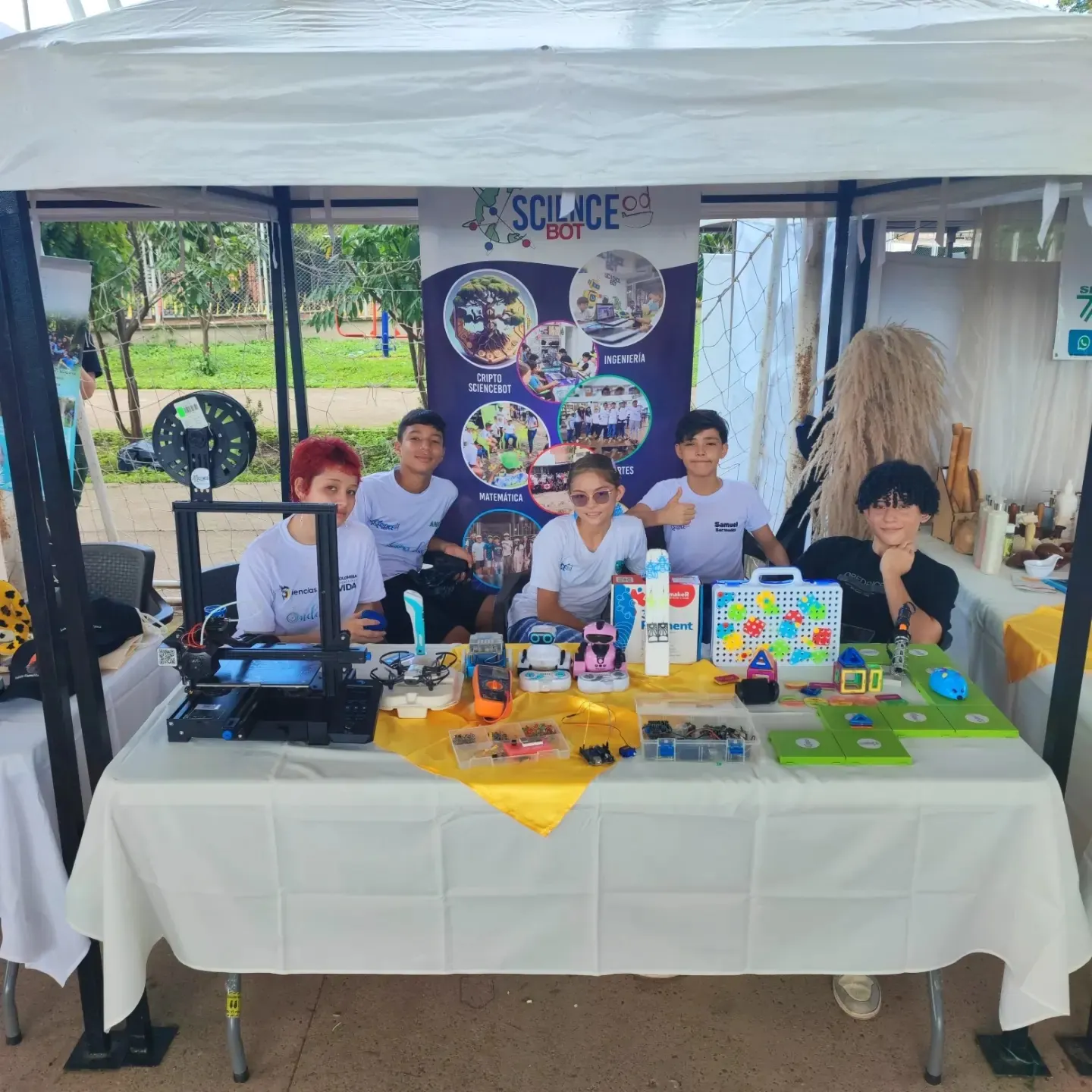 Stand de ScienceBot en una feria con impresoras 3D y estudiantes mostrando sus piezas